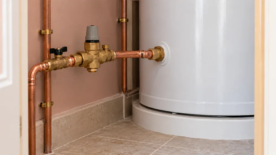 Pressure-reducing valve and supported copper cold-water inlet pipe beside an unvented hot-water cylinder.